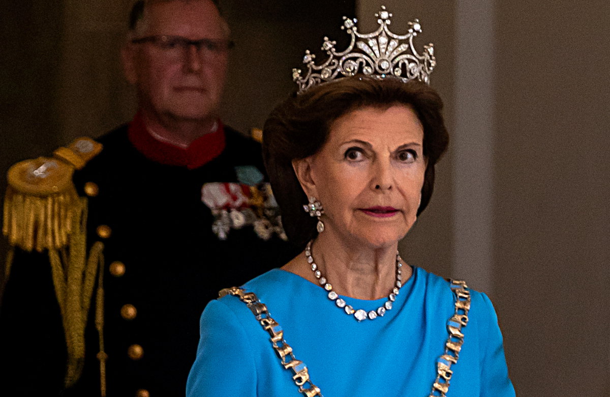 Königin Silvia von Schweden im königlichen Kostüm guckt konzentriert an der Kamera vorbei.