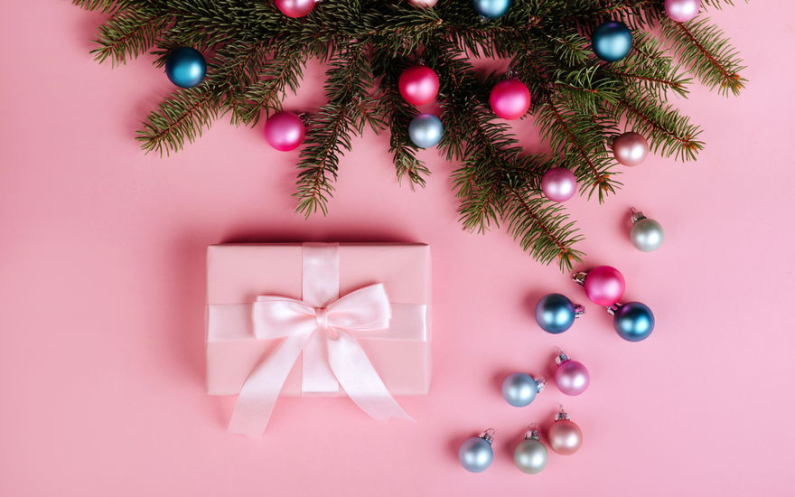 Geschenk auf rosa Hintergrund mit Tannenzweig und bunten Kugeln
