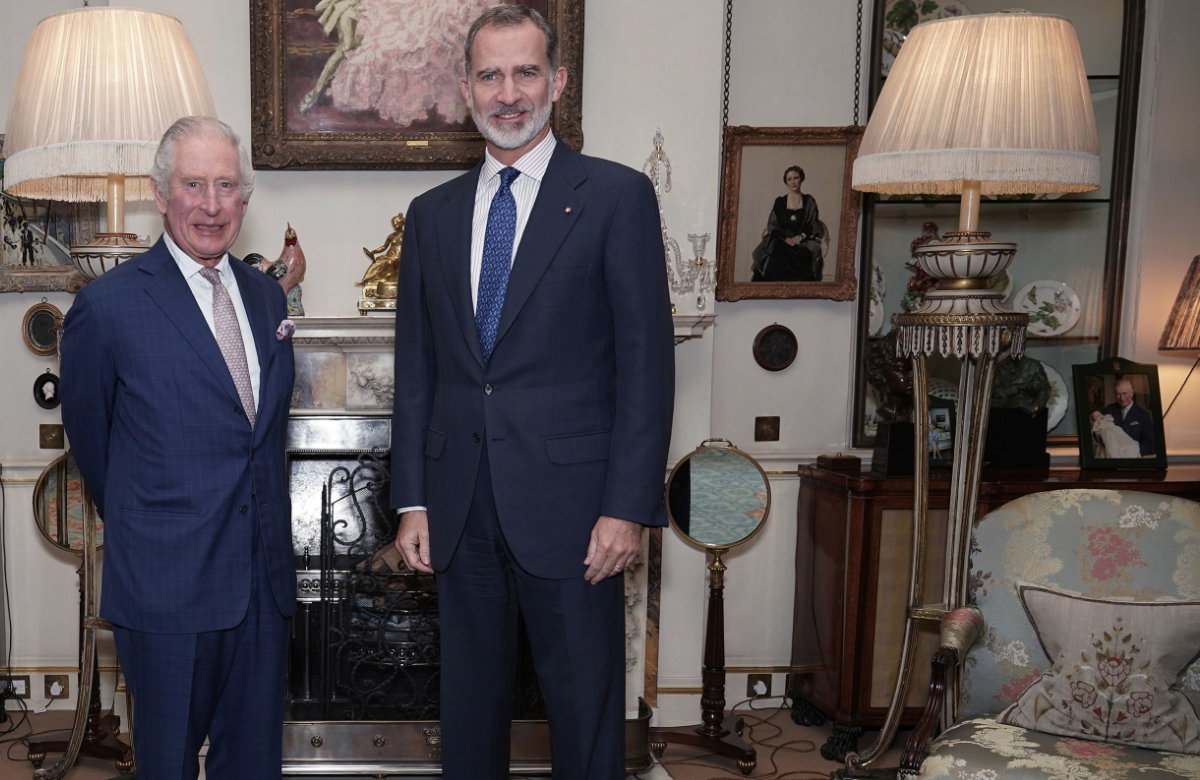 König Charles steht neben König Felipe und einem Bild von Prinz Georges Taufe