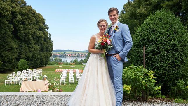 Sturm der Liebe Josie und Paul stehen in Brautkleid und Anzug vor einer Festwiese