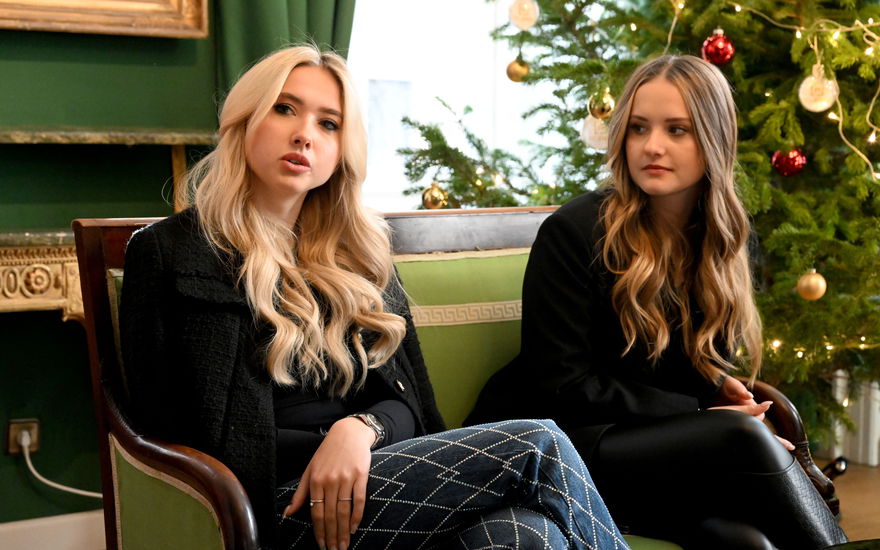 Davina und Shania Geiss sitzen auf einer Bank vor einem Weihnachtsbaum und gucken ernst