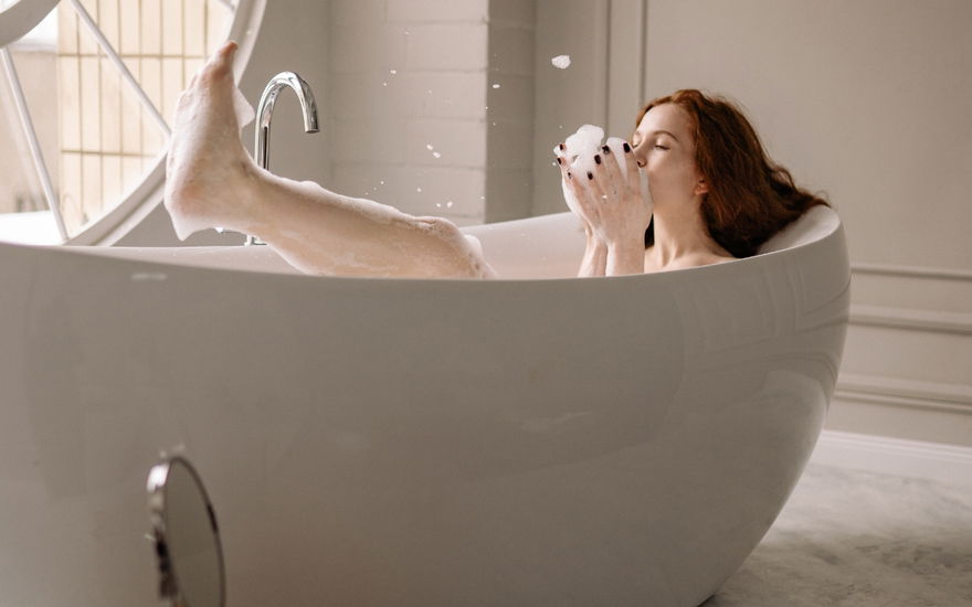 Rothaarige Frau liegt in Badewanne mit viel Schaum
