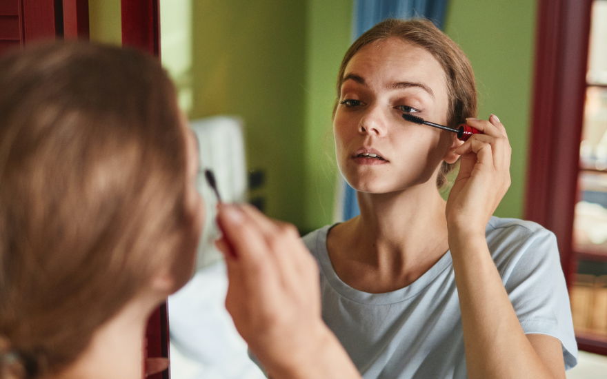 Frau trägt Mascara vor Spiegel auf