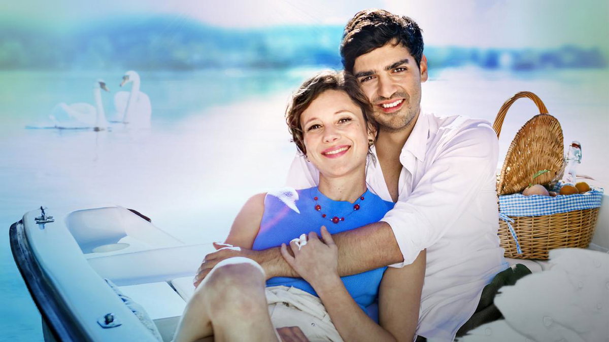 Sturm der Liebe Eleni und Leander liegen sich in den Armen im Boot neben ihnen ein Picknickkorb im Hintergrund ein See mit Schwänen