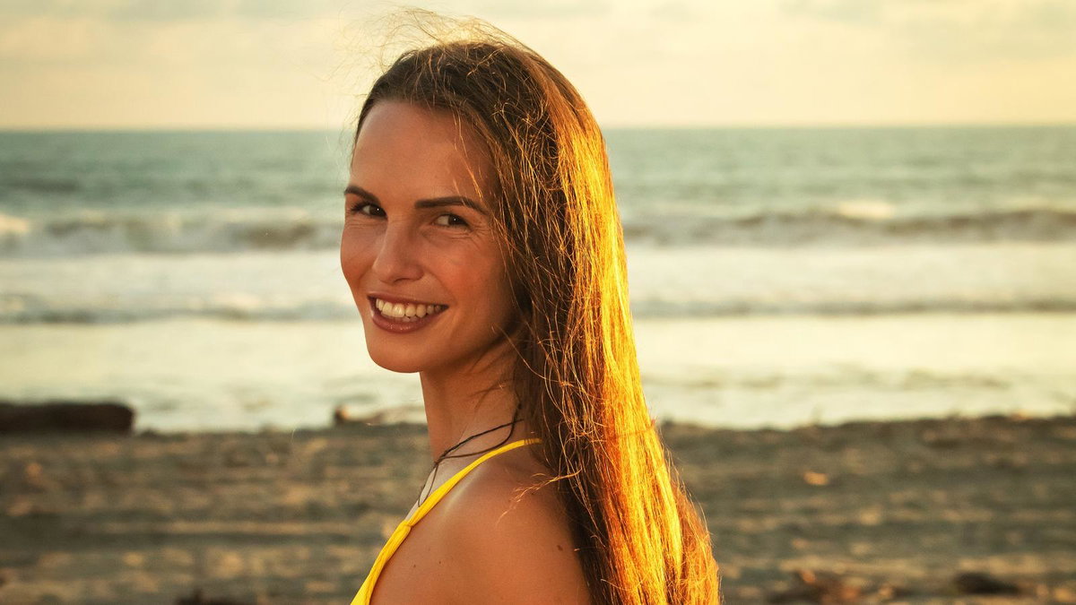 Bachelor 2023 Kandidatin Lisa M. steht am Strand und strahlt über die Schulter in die Kamera