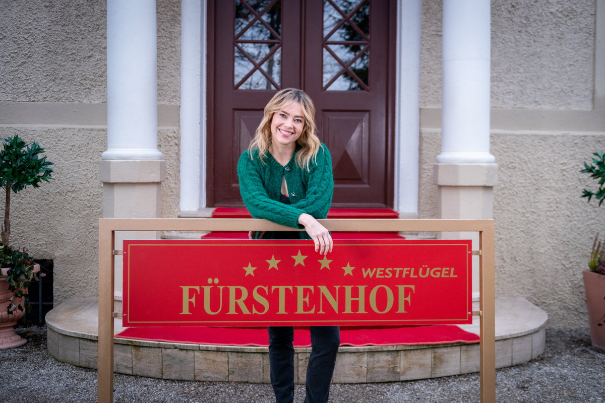 Greta Bergmann steht hinter dem Fürstenhof-Schild und lacht