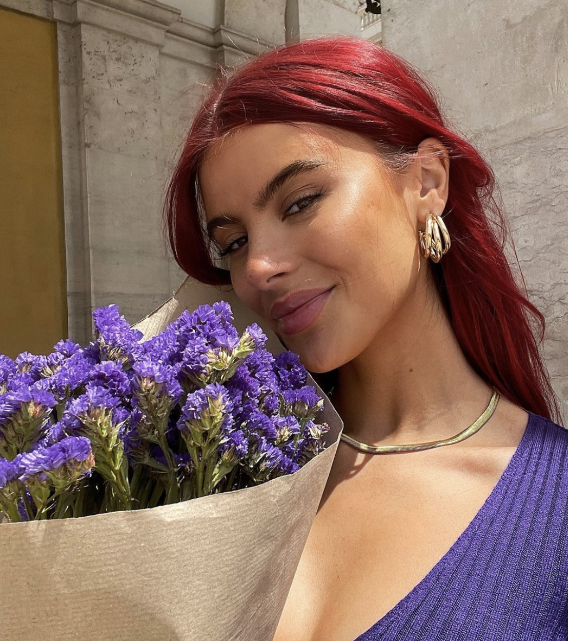 Romina Palm lächelt mit einem Strauß lila Blumen vor der Brust
