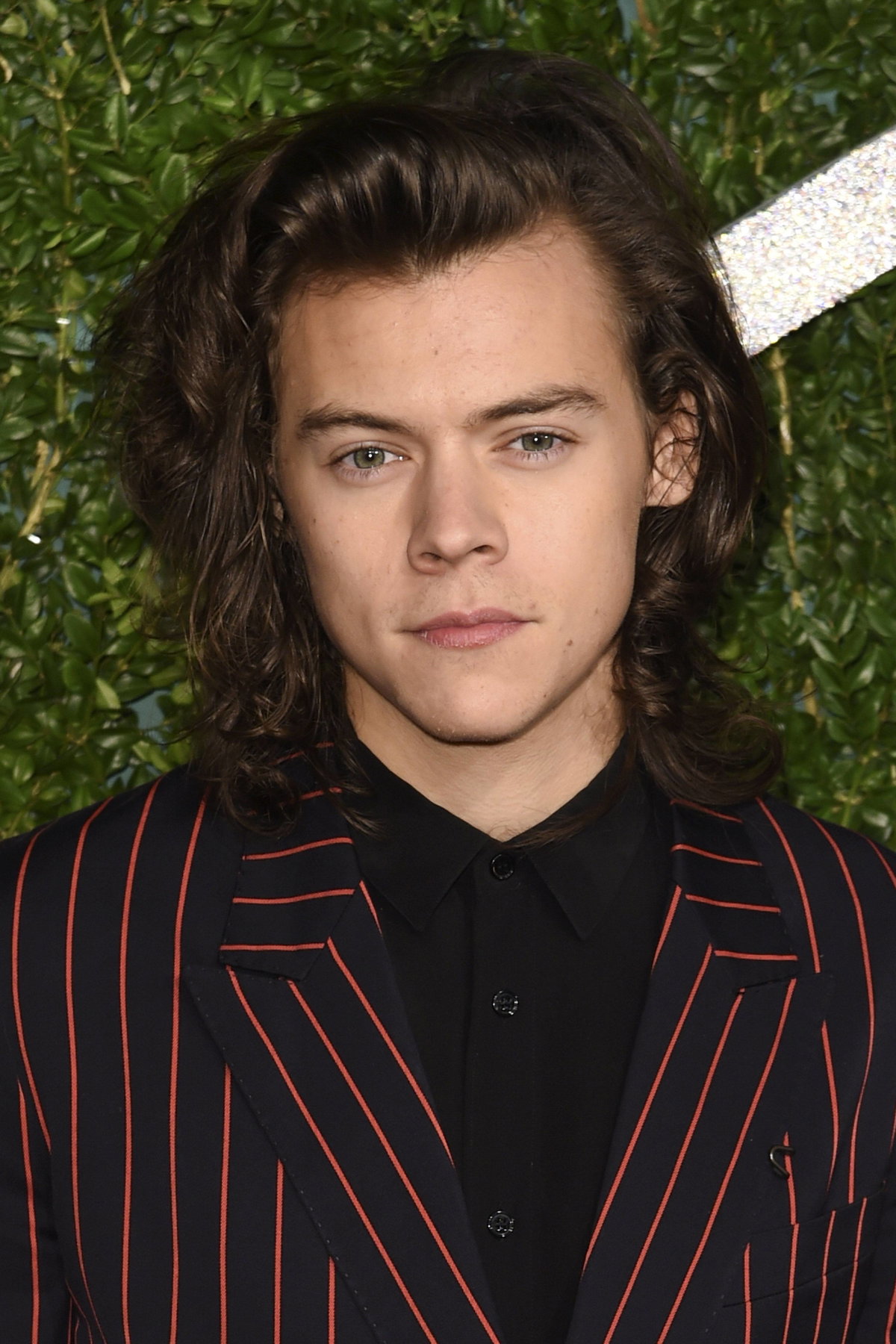 Harry Styles mit langen Haaren guckt ernst im Nadelstreifen-Anzug