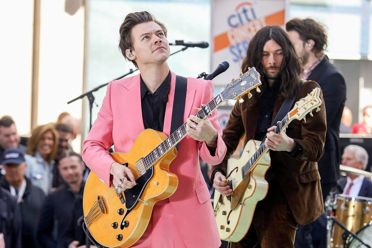 Harry Styles mit Gitarre in der Hand und pinken Anzug guckt hoch