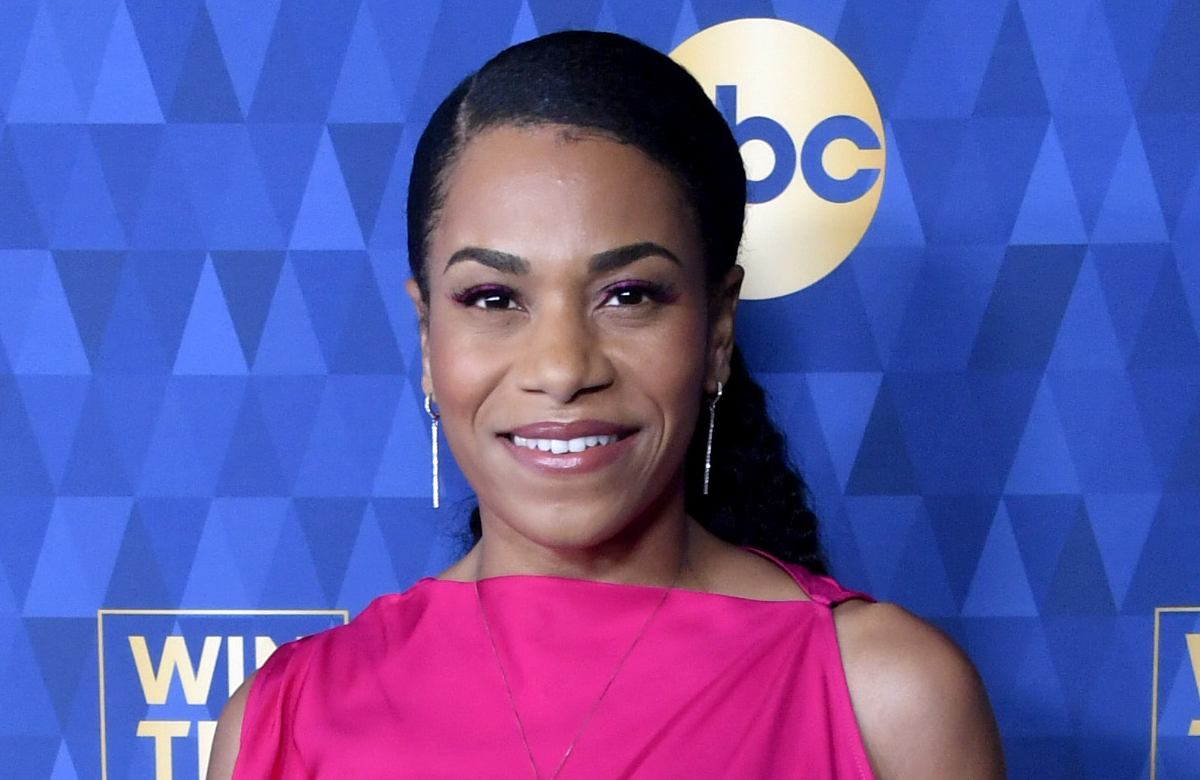 Kelly McCreary schaut lächelnd in die Kamera.