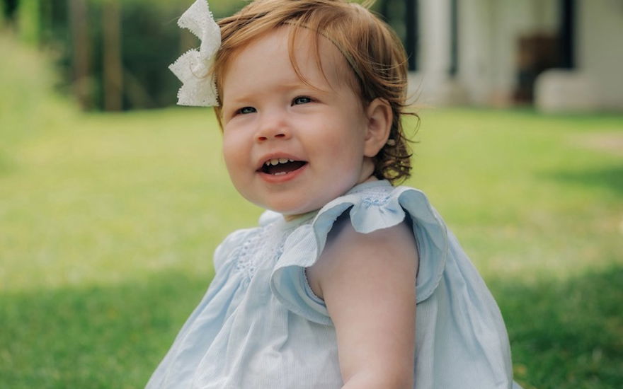Prinzessin Lilibet sitzt in einem blauen Kleid auf dem Rasen und lacht