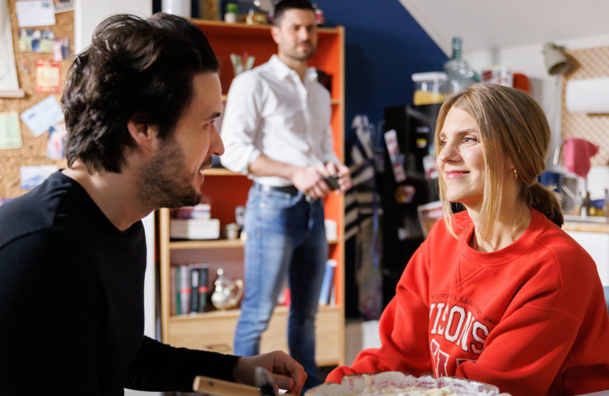 "Unter uns": Jakob und Stella am Tisch, gucken verliebt, Paco im Hintergrund