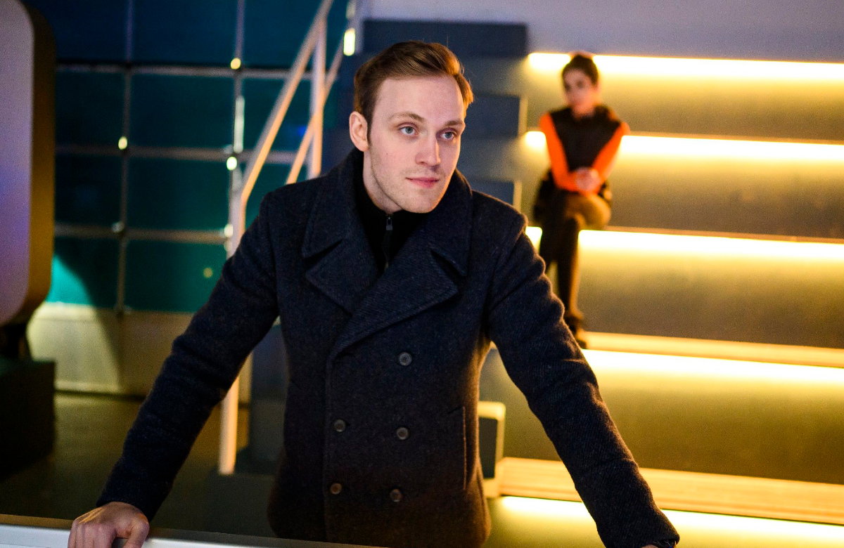 Luca steht bei "Alles was zählt" in der Eishalle, Leyla sitzt im Hintergrund auf den Treppen