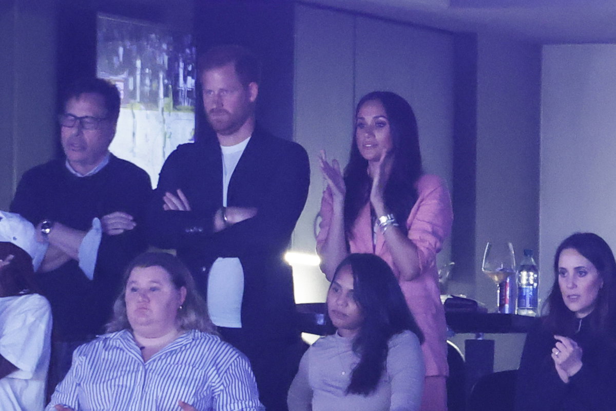 Prinz Harry und Herzogin Meghan stehen nebeneinander, sie klatscht
