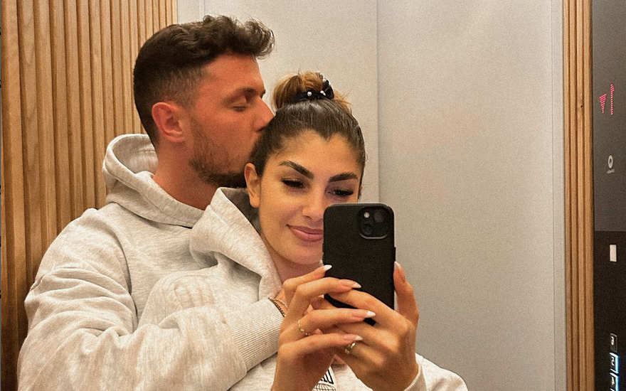 Yeliz Koc wird von hinten von Jannik Kontalis umarmt und bekommt einen Kuss auf die Wange während sie ein Selfie im Spiegel macht