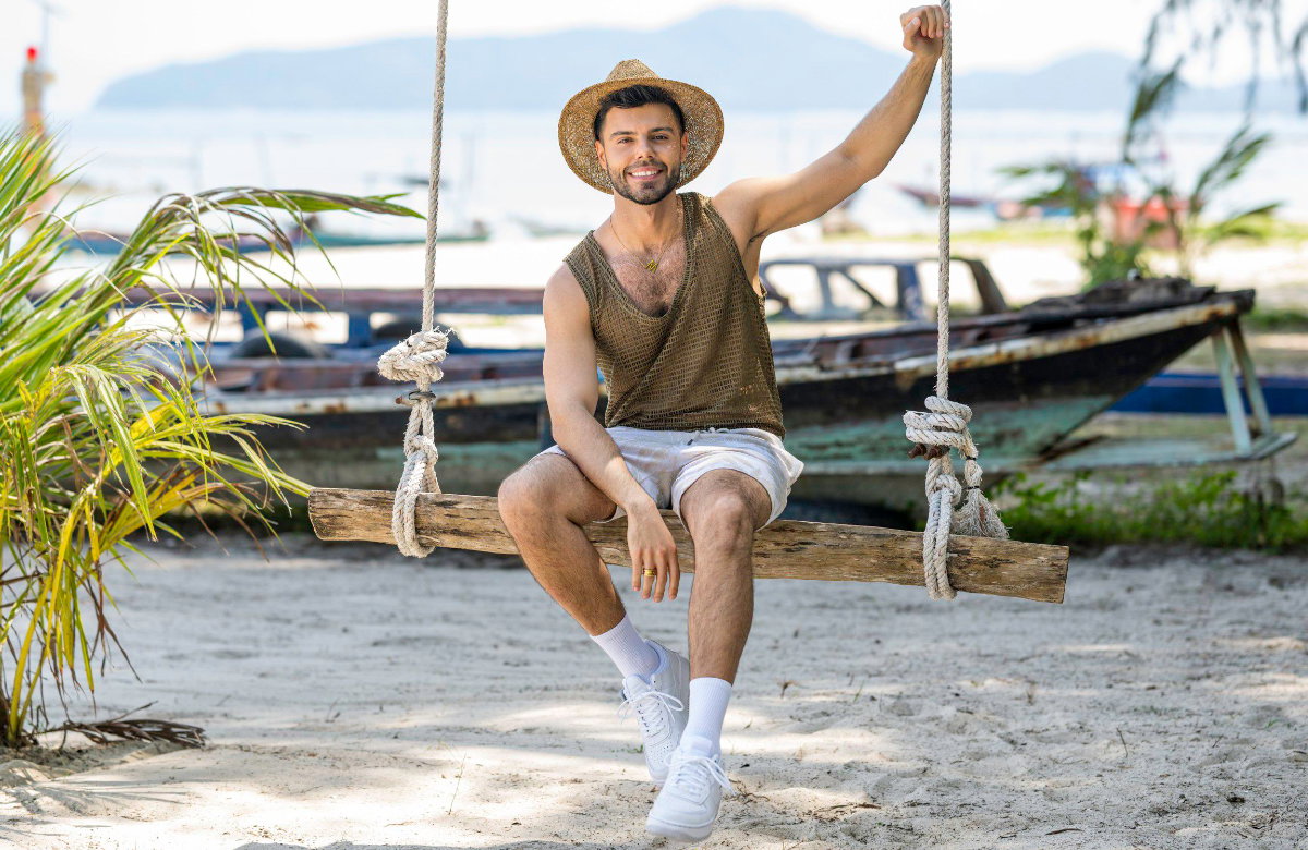 "Charming Boys"-Kandidat Martin Angelo lacht auf einer Schaukel am Strand