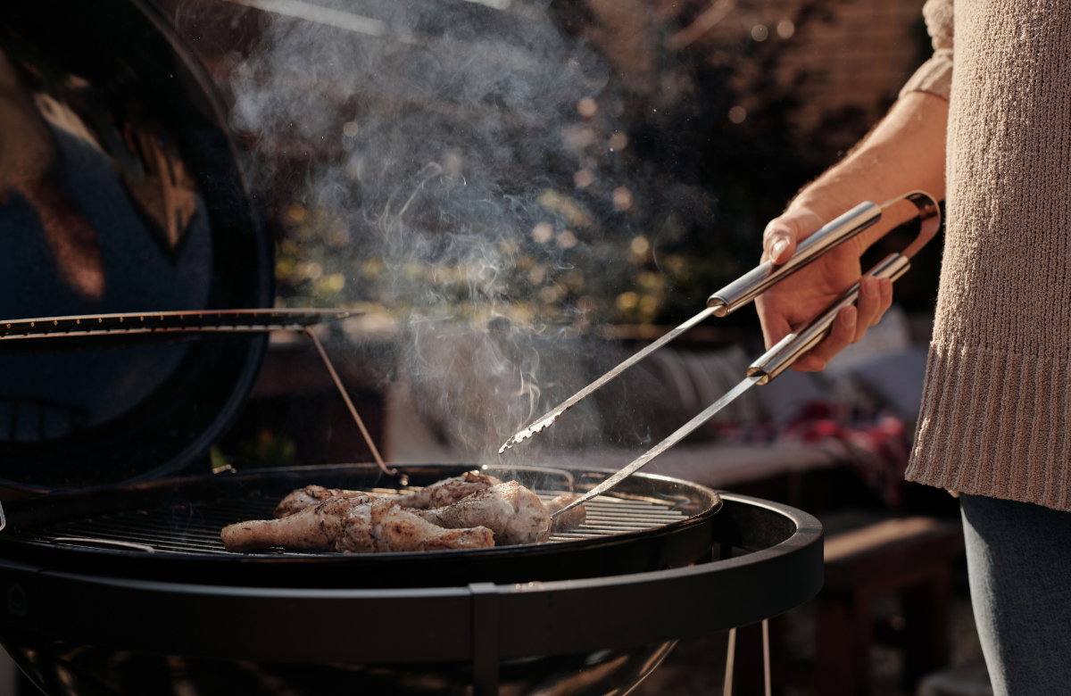 Frau grillt mit Grillzange in der Hand Hähnchen