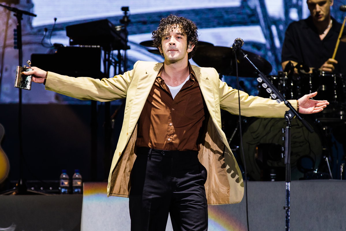 Matty Healy breitet die Arme auf der Bühne aus, in der Hand ein Flachmann