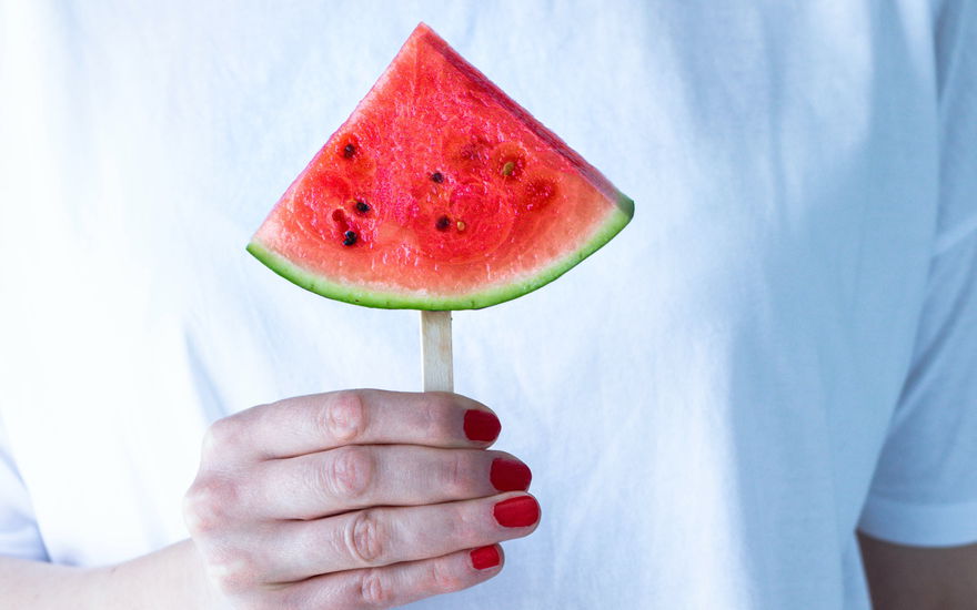 Rot lackierte Hand hält eine Wassermelone vor ein weißes Shirt