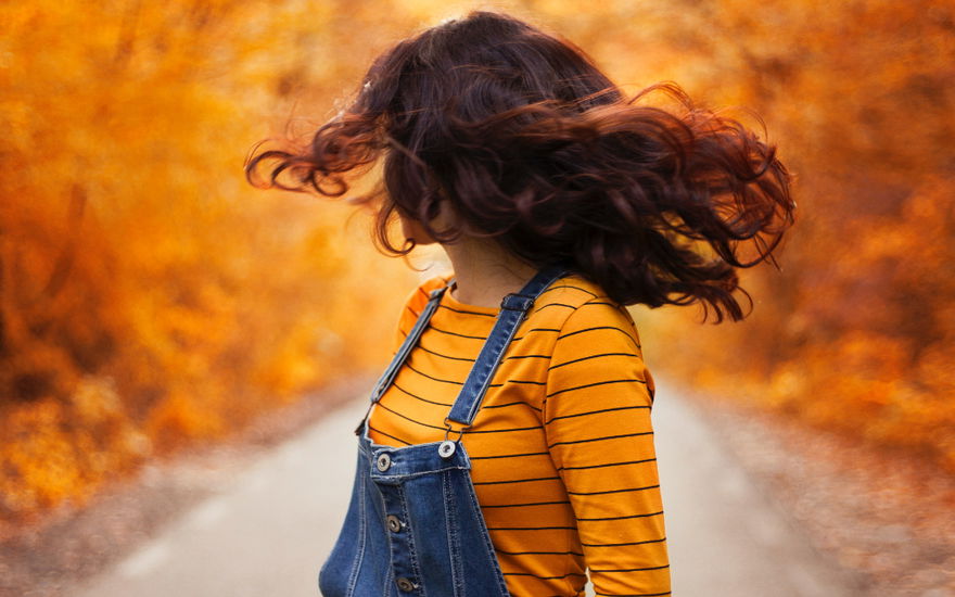Frau vor Herbst-Hintergrund schwingt Haare