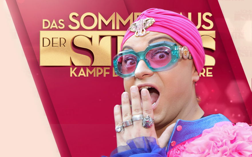 Julian F. M. Stoeckel guckt überrascht mit Hand vor dem Mund vor dem Logo von "Das Sommerhaus der Stars"