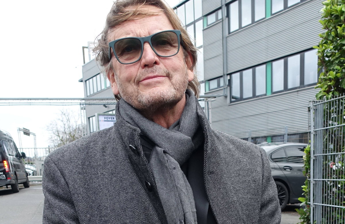 Peter Althof schaut ernst mit Sonnenbrille und Schal vor Gebäude