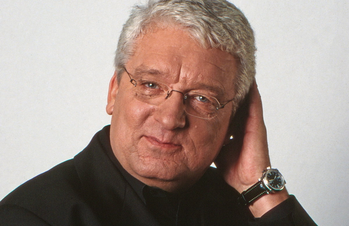 Hans Meiser lächelt mit Hand am Ohr