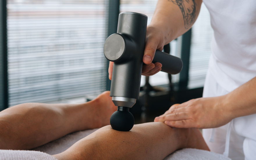 Hand hält massage-pistole und massiert damit waden von einem patienten