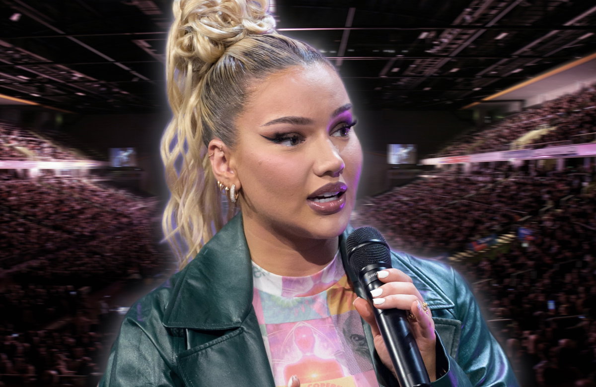Shirin David spricht am Mikrofon, im Hintergrund ist eine gefüllte Konzerthalle