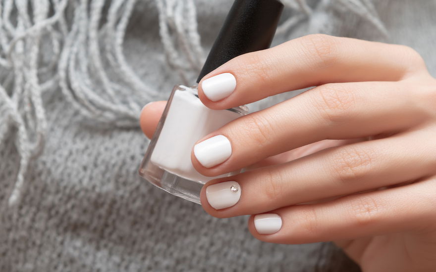 Frau mit weißem Nagellack in der Hand