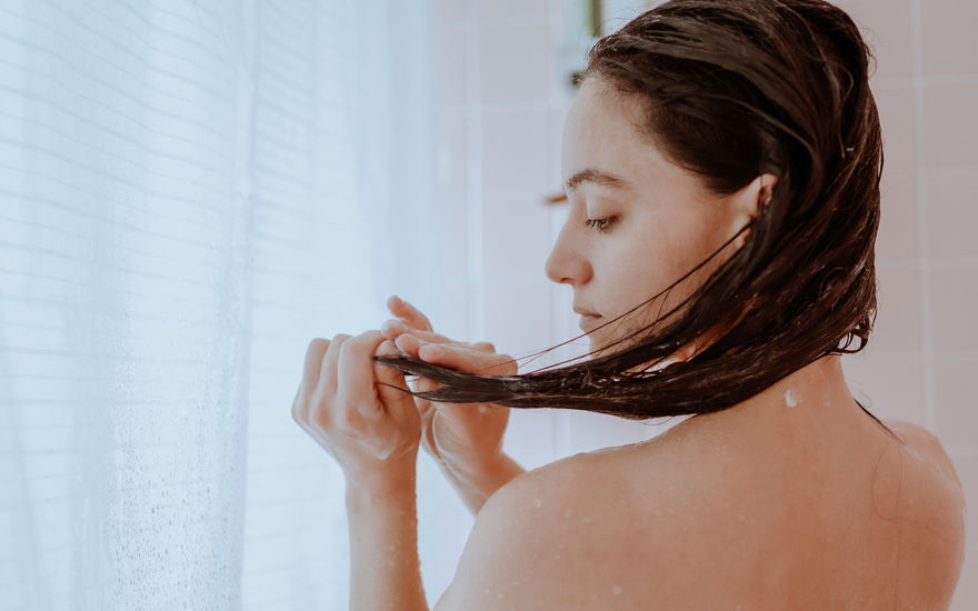 Frau mit Haarkur unter der Dusche
