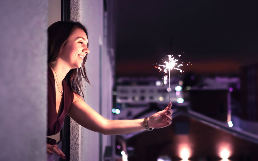 Frau hält Silvester allein eine Wunderkerze aus dem Fenster