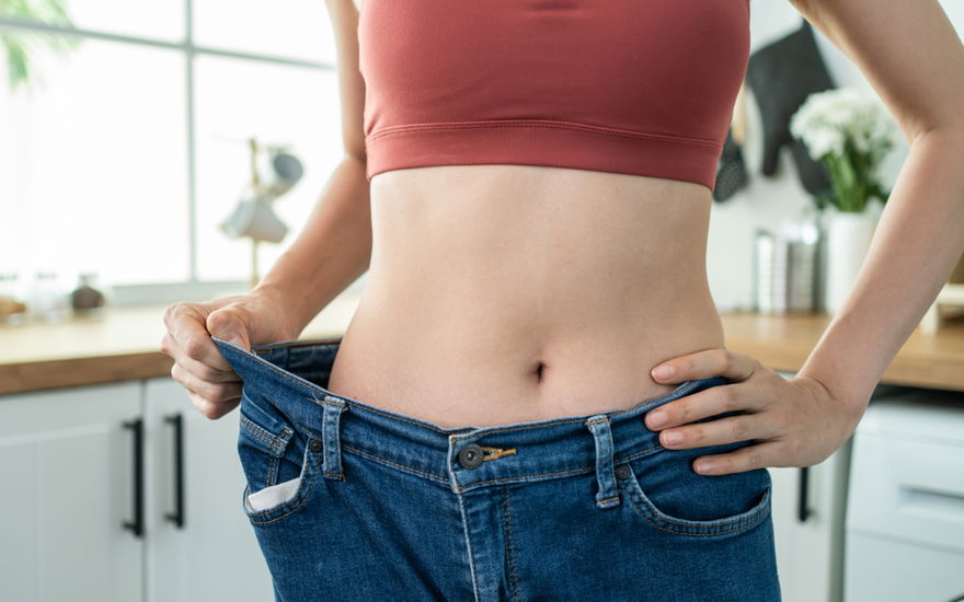 Frau zeigt nach Abnahme eine zu große Hose