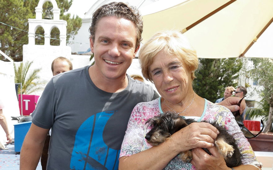 Stefan Mross lacht neben seiner Mutter Stefanie Mross, die einen Dackel auf dem Arm hat