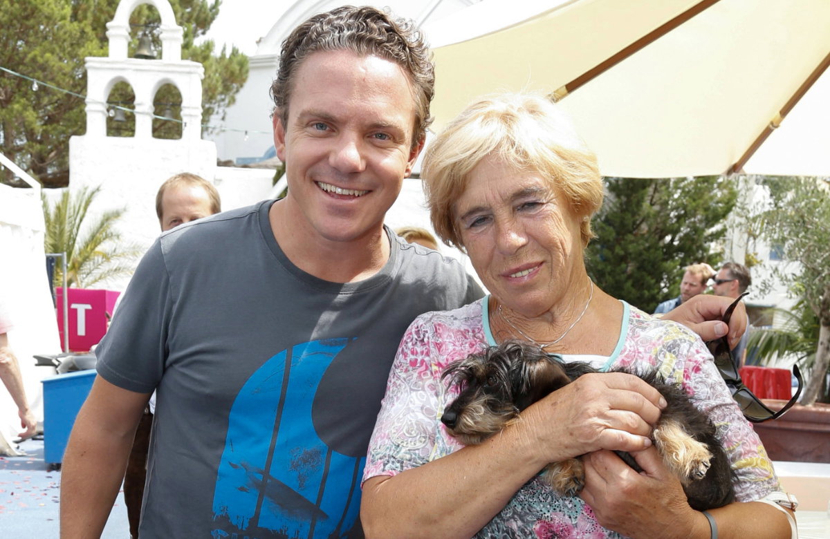 Stefan Mross lacht neben seiner Mutter Stefanie Mross, die einen Dackel auf dem Arm hat