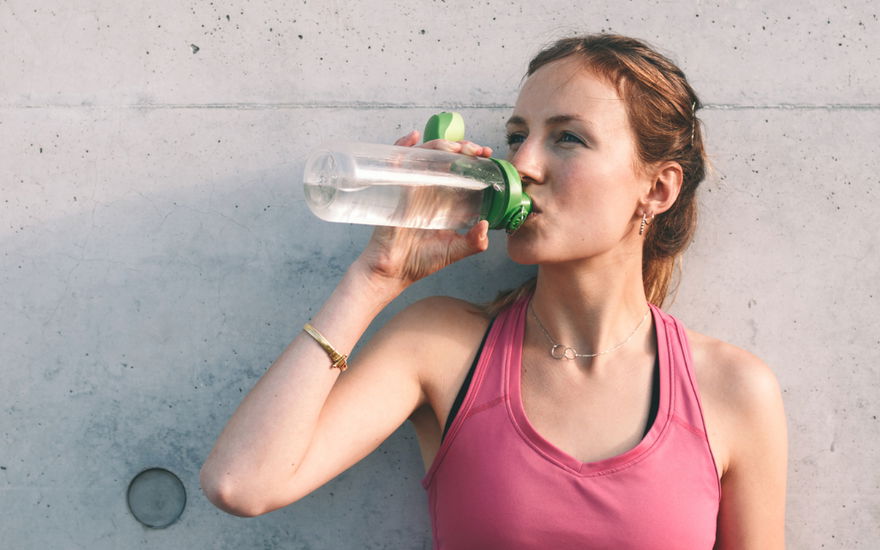 Frau in sportlichen Top trinkt aus einer Flasche