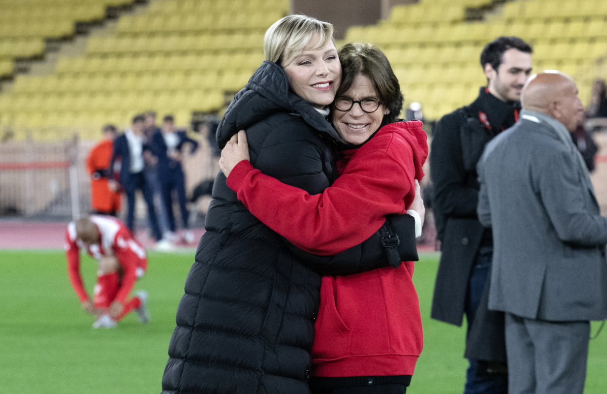 Fürstin Charlène und Prinzessin Stéphanie umarmen sich bei einem Fußballspiel.