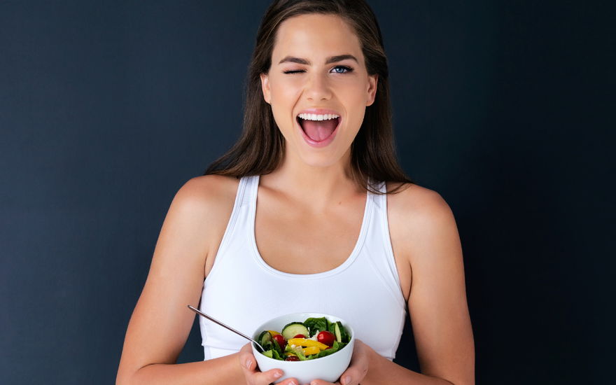schlanke Frau hält veganen Salat vor sich