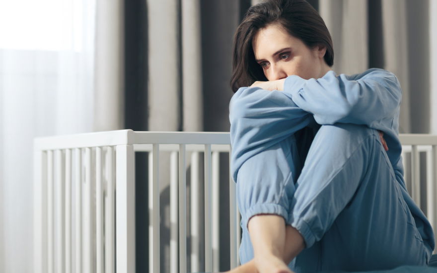 Frau sitzt traurig vorm Babybett