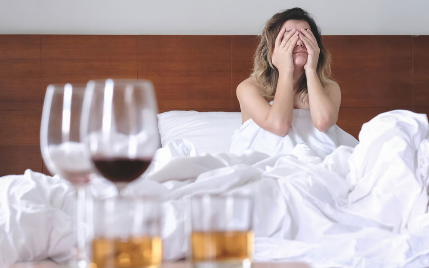 frau sitzt verkatert im bett und hält sich den kopf