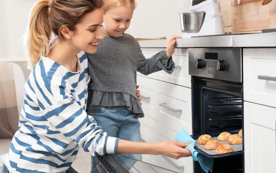 Mutter und Tochter öffnen Backofen mit Brötchen auf einem Backpapier Ersatz
