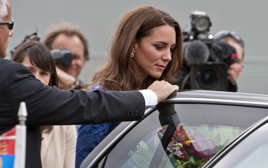 Prinzessin Kate steigt in ein Auto, ein Sicherheitsmann hält ihr die Tür auf. Im Hintergrund haben sich Paparazzi versammelt.