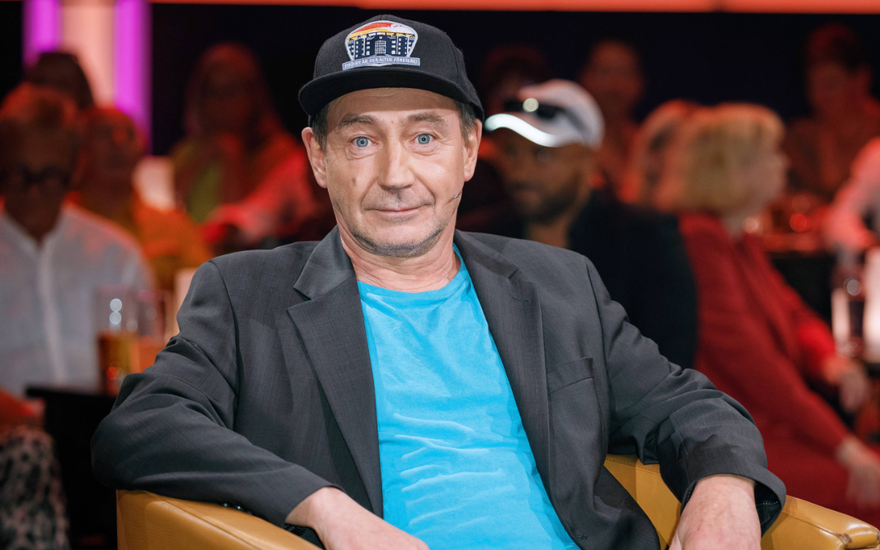 Thorsten Merten sitzt auf einem Sessel, im Hintergrund Menschen