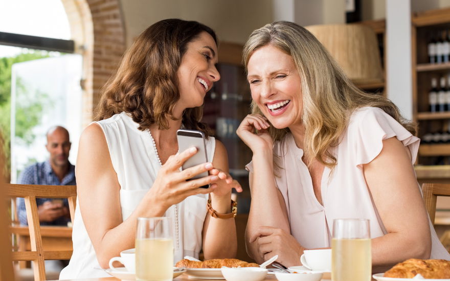 zwei modische frauen gucken zusammen aufs Handy und lachen