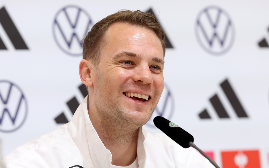 Manuel Neuer lacht in einer Trainingsjacke bei einer Pressekonferenz