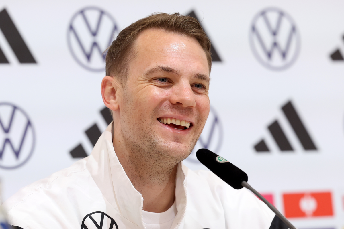 Manuel Neuer lacht in einer Trainingsjacke bei einer Pressekonferenz