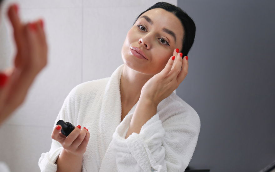 Frau vor Spiegel mit Anti-Aging-Serum
