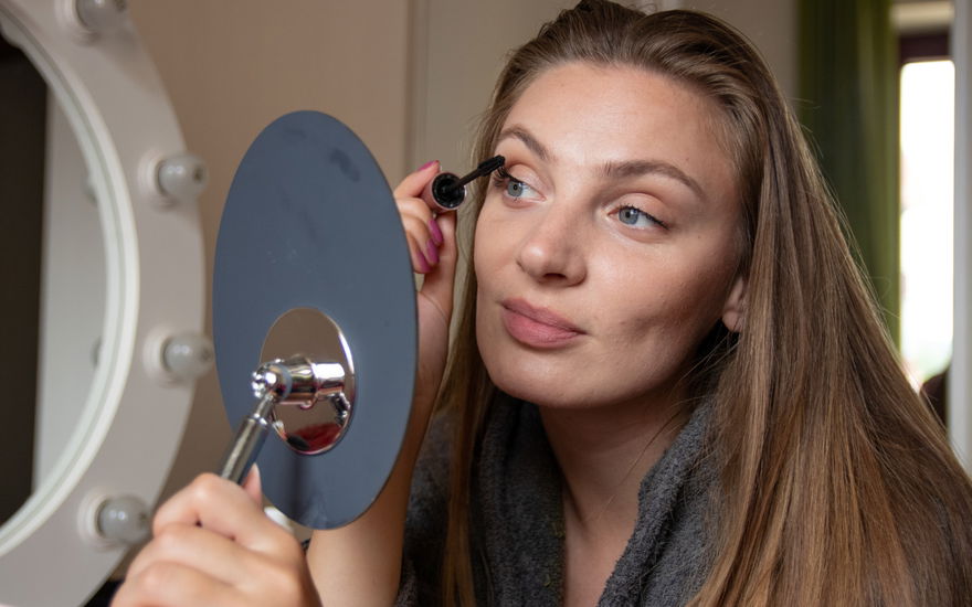 Frau tuscht Wimpern vor Spiegel