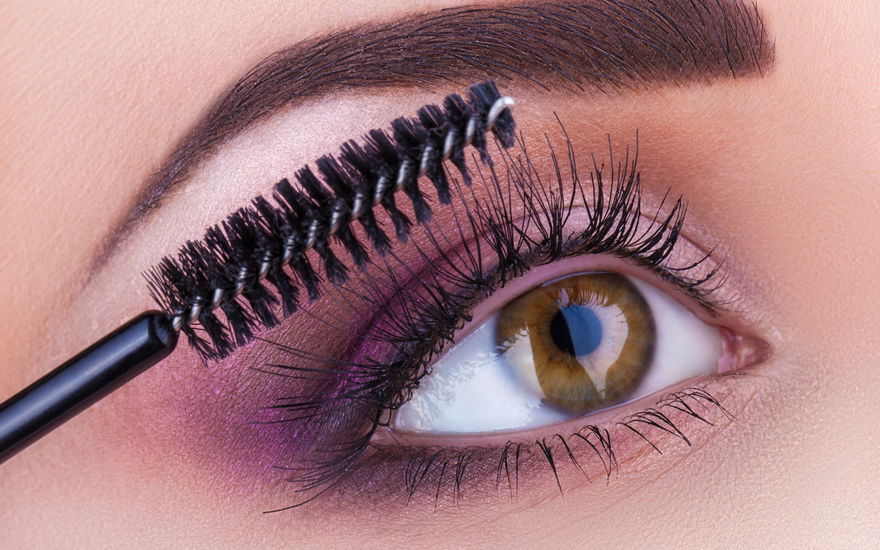 Frau mit lila Lidschatten tuscht Wimpern