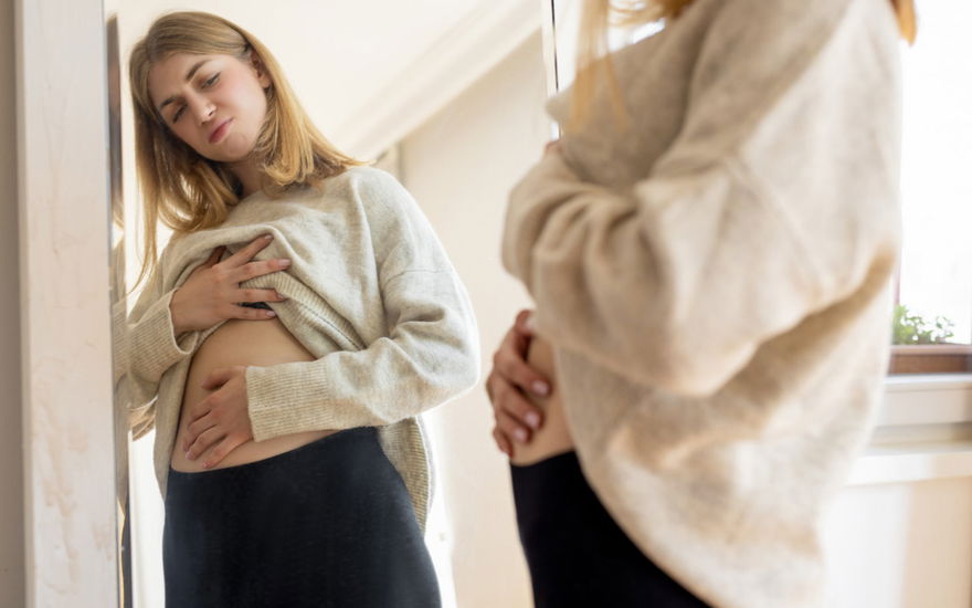 Frau schaut Bauch im Spiegel an